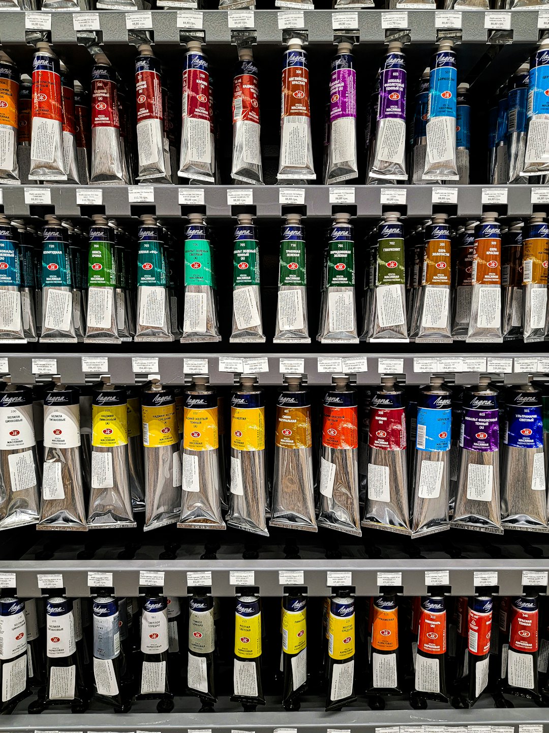 Fila di tubetti di vernice artistica colorata su scaffali espositivi da negozio.